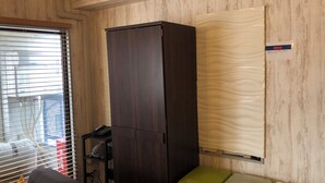 Una habitación con un armario de madera oscura, un bote de basura verde y un caja de almacenamiento color beige.