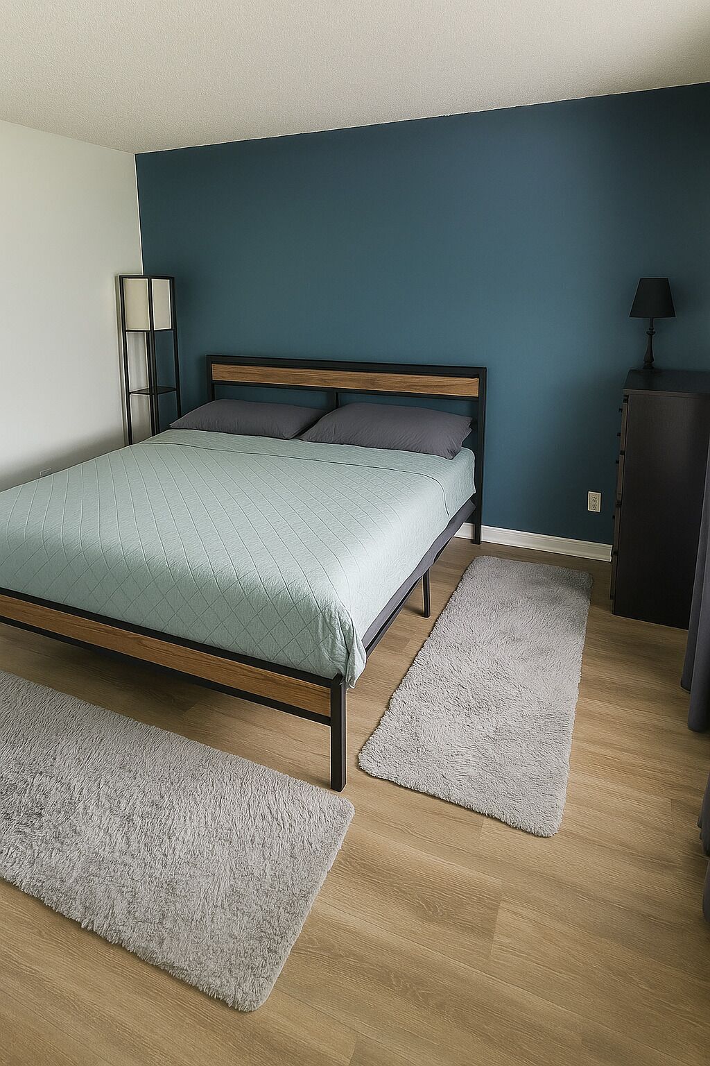 A bedroom with a bed, two rugs, a nightstand, a lamp, and a dresser.