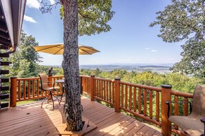 Um deck de madeira com vista para um vale, um corrimão de madeira e uma mesa com cadeiras.