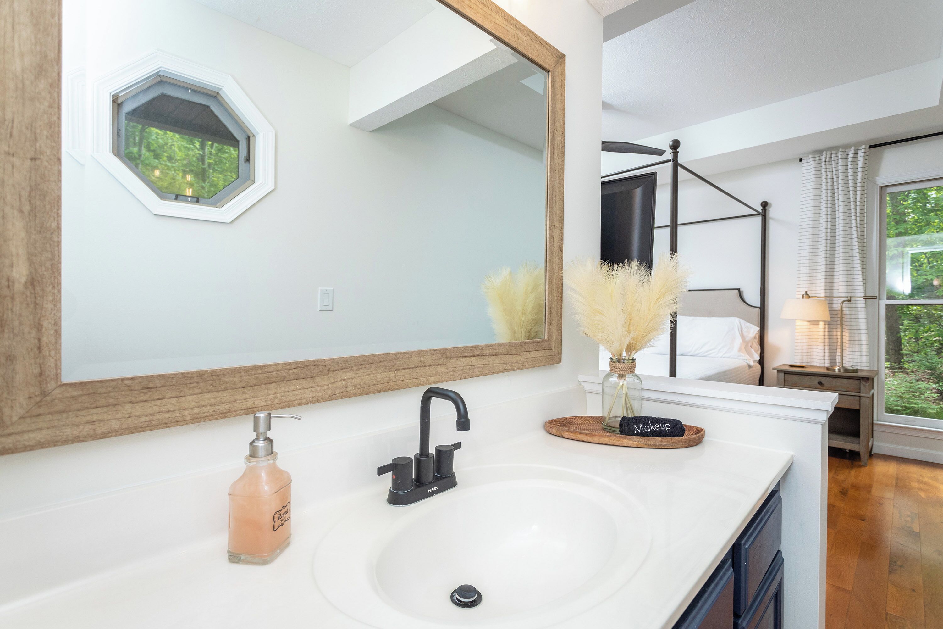 A bathroom with a white sink, a large mirror, and a window with a view of trees.