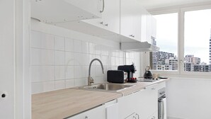 Une cuisine moderne avec des meubles blancs, un évier en acier inoxydable et une fenêtre donnant sur un paysage urbain.