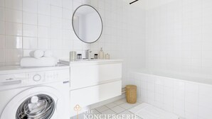 Une salle de bain moderne équipée d’un lave-linge, d’un meuble-lavabo avec des articles de toilette et d’une baignoire.