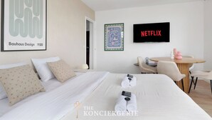 Une chambre d’hôtel avec un lit, des oreillers, une télévision, un tableau encadré et une table avec des chaises.