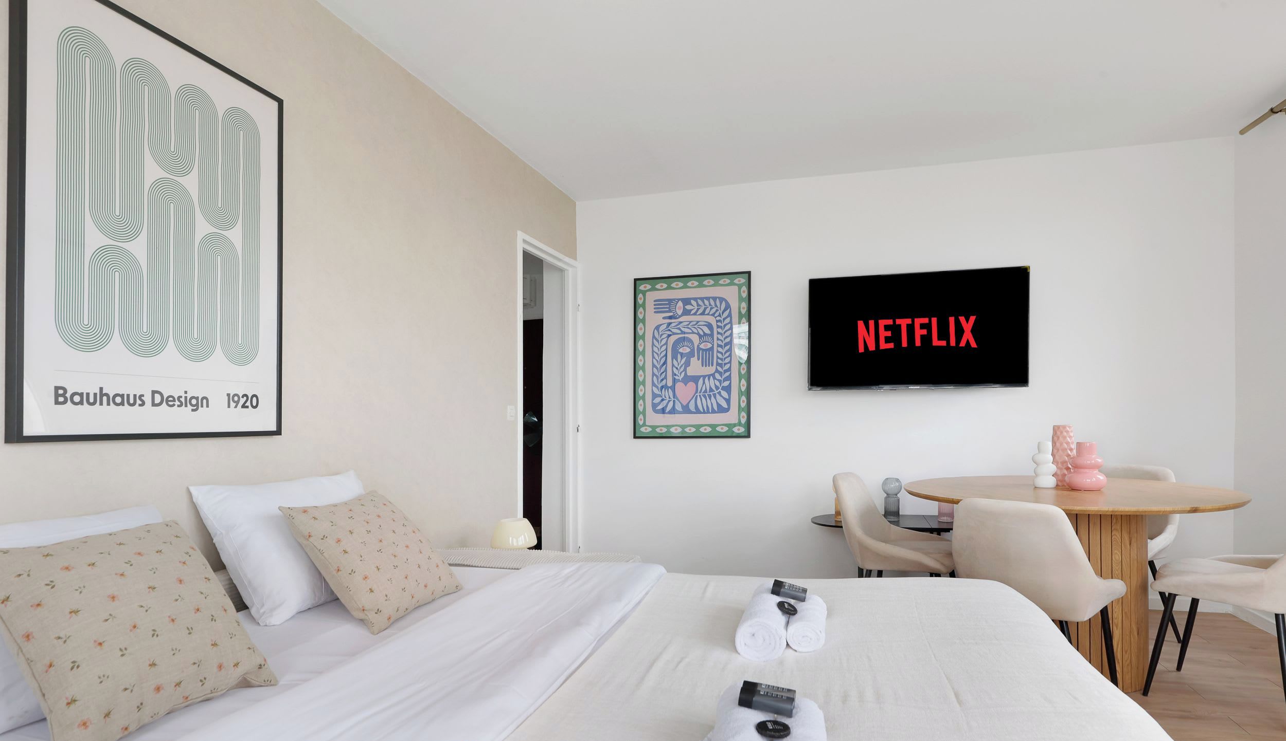 Une chambre d’hôtel avec un lit, des oreillers, une télévision, un tableau encadré et une table avec des chaises.
