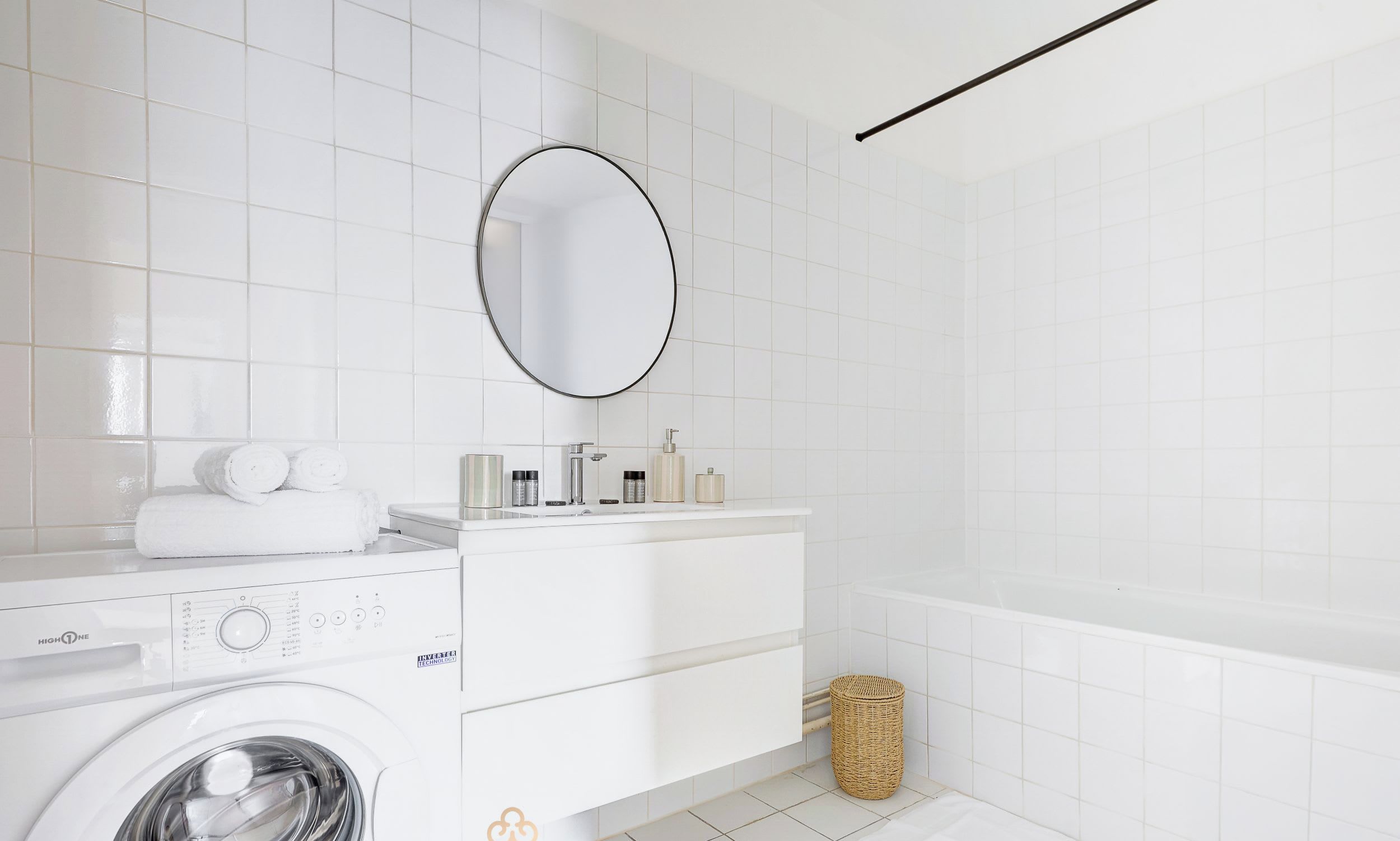 Une salle de bain moderne équipée d’un lave-linge, d’un meuble-lavabo avec des articles de toilette et d’une baignoire.