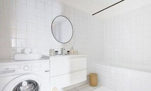 A modern bathroom with a washing machine, a vanity with toiletries, and a bathtub.