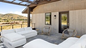 A modern outdoor seating area with white sofas and wicker chairs, a wooden pergola, and a view of the countryside. - Luxury Retreat 12 miles from Park City - Ameyalli (Midway)