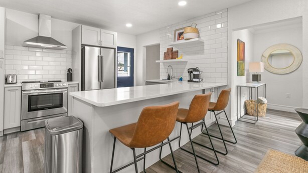 A modern kitchen with white cabinetry, stainless steel appliances, a central island with bar stools, and a blue door leading to another room. - NEW Soho Sanctuary - Gorgeous Apartment Steps to S Howard Ave With Fenced Yard (Tampa)