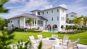 Une grande maison blanche avec une piscine, un espace salon extérieur et un hamac.