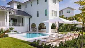 Une grande maison blanche dotée d’une piscine, d’un espace salon extérieur et d’un patio couvert.