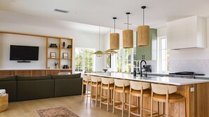 Une cuisine moderne dotée d’un îlot central, de tabourets de bar, de luminaires suspendus et d’un téléviseur encastré.