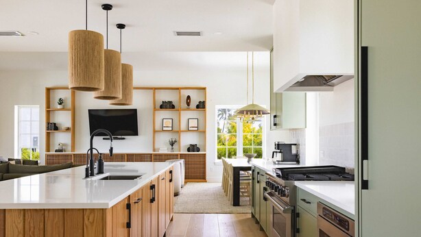 Une cuisine moderne dotée d’un îlot central, de meubles en bois, d’un four encastré et d’une grande fenêtre qui laisse entrer la lumière naturelle.