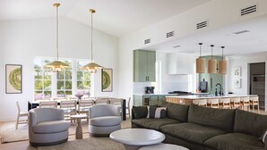 Un salon moderne avec un canapé vert, deux petites tables rondes blanches et un coin repas comprenant une table et des chaises.