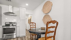 A modern kitchen with white cabinetry, a stainless steel stove, and a round dining table with wooden chairs. - NEW Soho Home - Perfect Space for Families (Tampa)