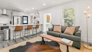 A modern kitchen with white cabinets, a stainless steel refrigerator, and a bar area with stools. - NEW Soho Home - Perfect Space for Families (Tampa)