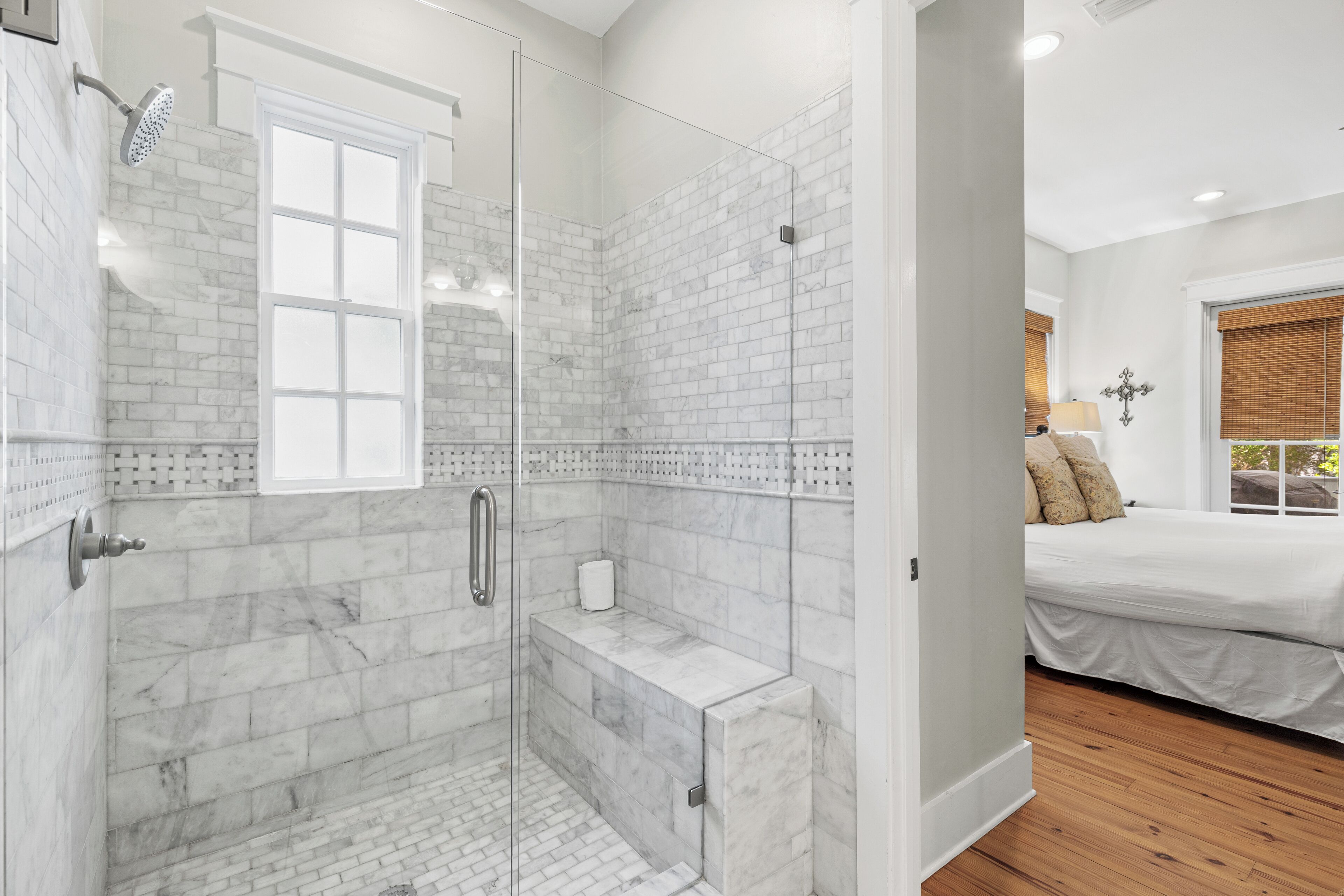 A modern bathroom with a glass-enclosed shower, marble tiles, and a wooden floor.