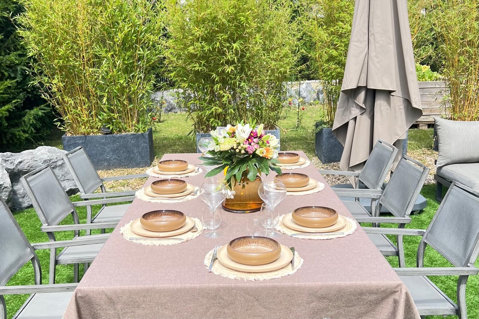 Un espace de restauration en plein air avec une table dressée pour six personnes, entourée de chaises, et agrémenté d’un arrangement floral en guise de centre de table.