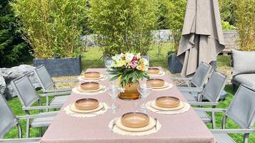 Un espace de restauration en plein air avec une table dressée pour six personnes, entourée de chaises, et agrémenté d’un arrangement floral en guise de centre de table.