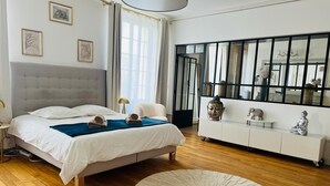 Quarto moderno com uma cama grande, uma mesa de cabeceira, um console branco, um tapete redondo e uma janela ampla com cortinas.