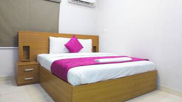 A neatly made bed with white bedding and a pink blanket, a wooden headboard, and a nightstand with drawers.