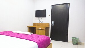 A hotel room with a bed, a wooden desk, a television mounted on the wall, and a black door. - Clean Single Room in Lagos Suitable for Getaway and Remote Work (Yaba)