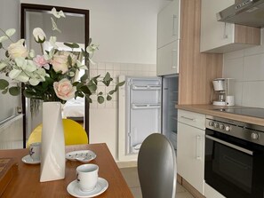 Cozinha moderna com geladeira, forno e cafeteira. Há um vaso com flores na mesa.