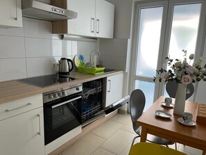 Uma cozinha moderna com armários brancos, forno embutido e área de refeições com mesa e cadeiras.