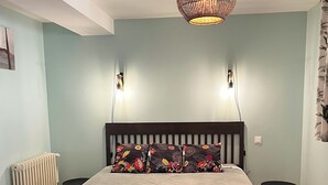 Quarto com cama, mesas de cabeceira, um banco, radiador e luminária pendente.