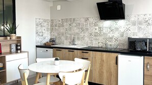 Uma cozinha moderna com uma mesa de jantar redonda, cadeiras de madeira, lava-louças embutida e uma TV preta fixada na parede.