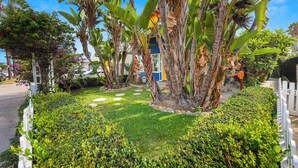 A well-maintained garden with banana trees, a white picket fence, and a paved pathway. - Private 3 Bed House in North Park • Work, Yard, EV (San Diego)