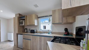 Una cuina moderna amb armaris de fusta, un microones, una rentavaixelles, una placa de cocció i una finestra amb vista a una casa.