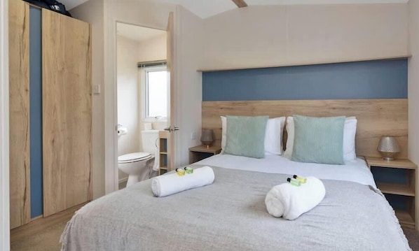 A hotel room with a bed, a wooden headboard, a nightstand, a bedside table, and a bathroom visible through an open door. - Vacant Nests | Seton sands | St Andrews (Longniddry)