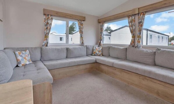 A modern living room with a grey sectional sofa, wooden floor, and large windows with curtains.