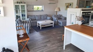 A modern living room with striped sofas, a white coffee table, and a wooden dining table. There is a kitchen area with an oven and a window. - 4 Star Holiday Home in Karrebaeksminde (Karrebæksminde)