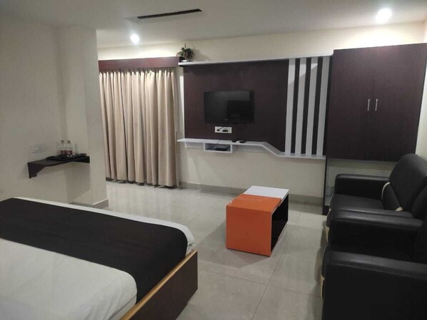 A hotel room with a bed, a TV mounted on the wall, a desk, a chair, and a wardrobe. - HOTEL NARMADA GRAND (Tadepalle)