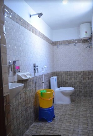 A bathroom with a toilet, a sink, and a shower. There is a yellow and blue bucket on the floor. - HOTEL NARMADA GRAND (Tadepalle)