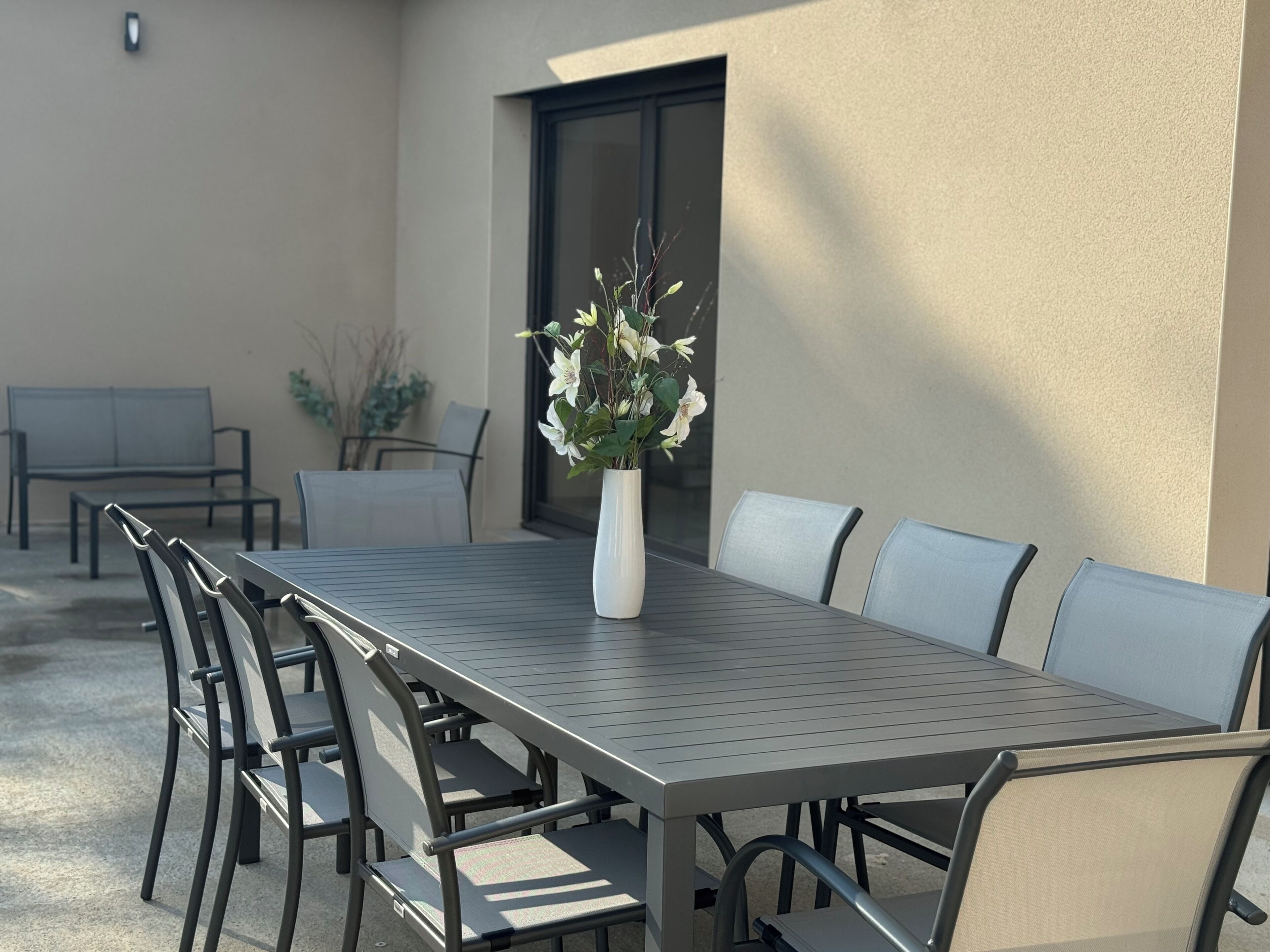 Une terrasse extérieure avec une table et des chaises en métal, une plante en pot et une fenêtre.