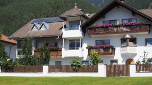A two-story building with a sloped roof, balconies with flower boxes, and a white facade. - Appartment with beautiful mountain view (San Giorgio)