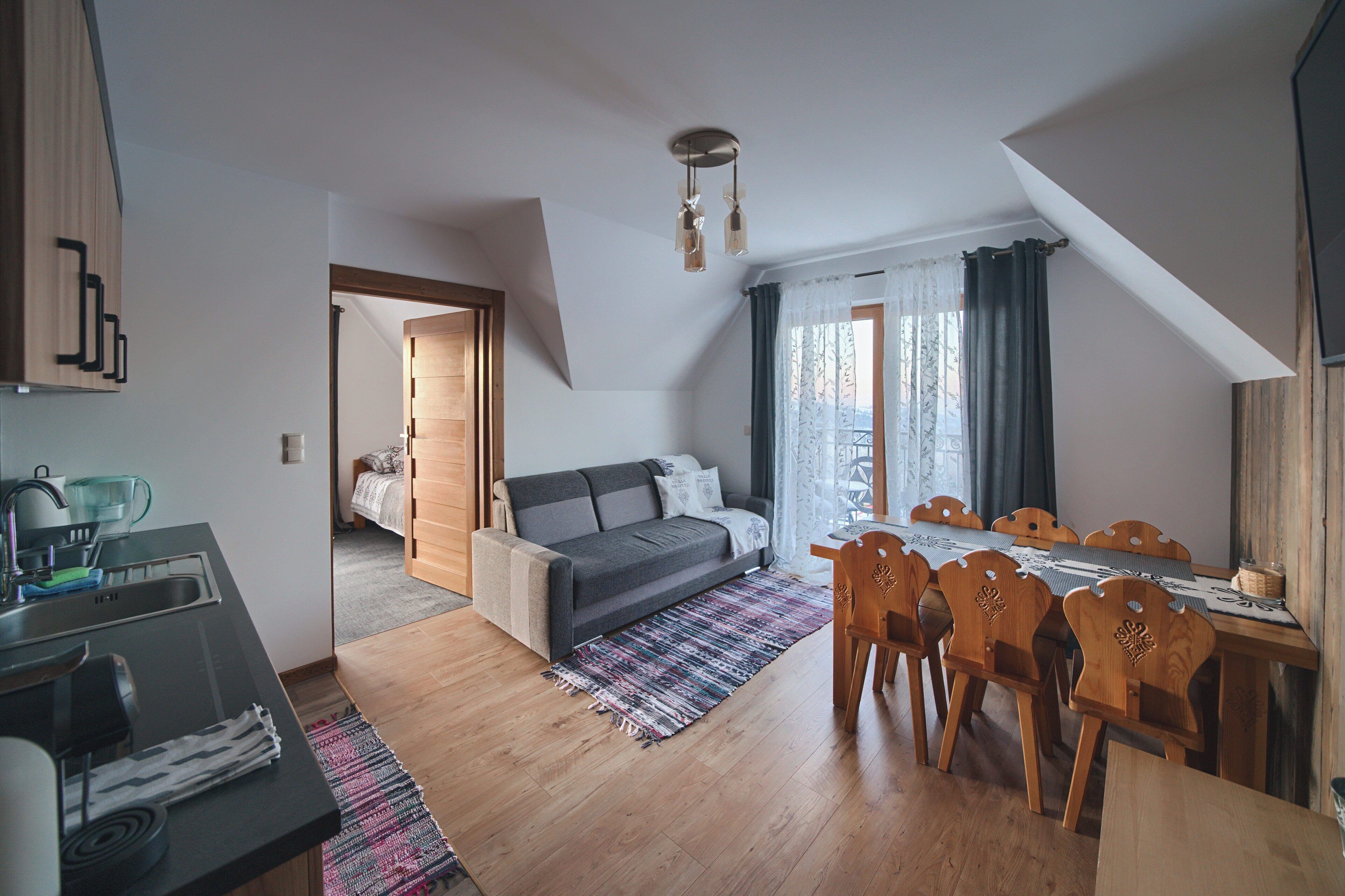 A compact living space with a kitchenette, a sofa, a dining table with chairs, and a large window with curtains.