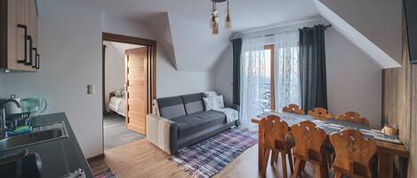 A compact living space with a kitchenette, a sofa, a dining table with chairs, and a large window with curtains.