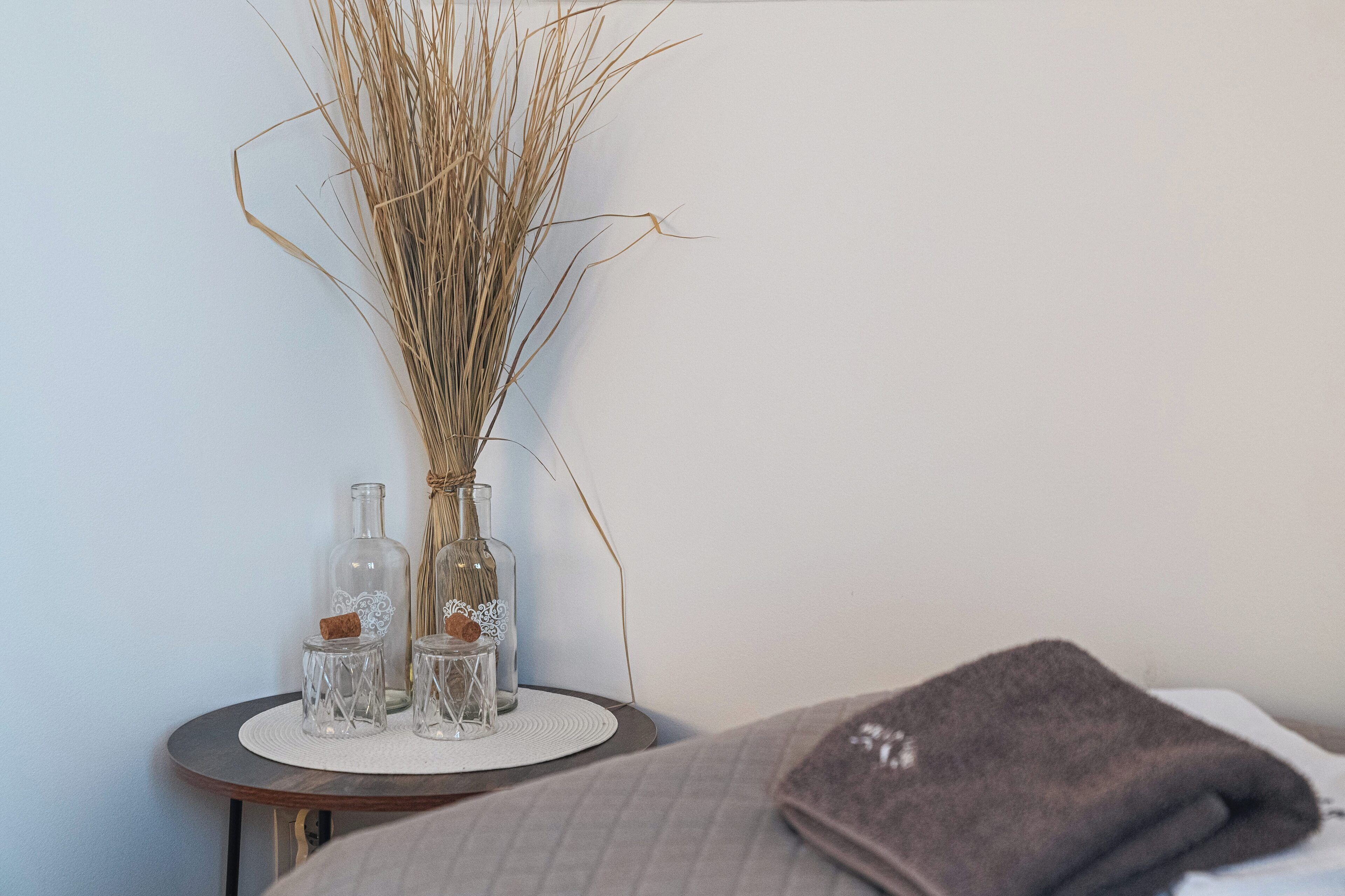 A neatly arranged bedside table with a vase of dried reeds, two clear glass bottles, and a small decorative item.