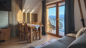 Ein gemütliches Zimmer mit einem Holzesstisch und -stühlen, einer Couch und Blick auf Berge durch eine große Glasschiebetür.