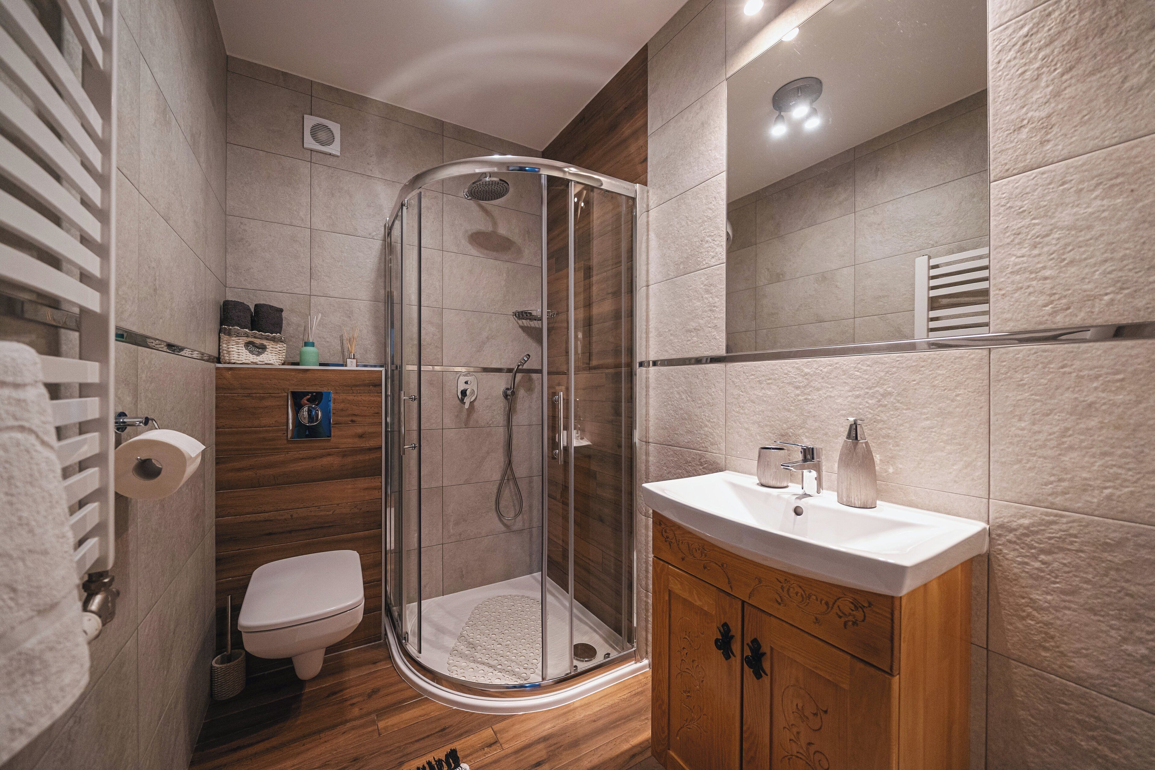 Ein modernes Badezimmer mit einer in Glas eingefassten Dusche, einem Holzwaschtisch und einer Toilette.
