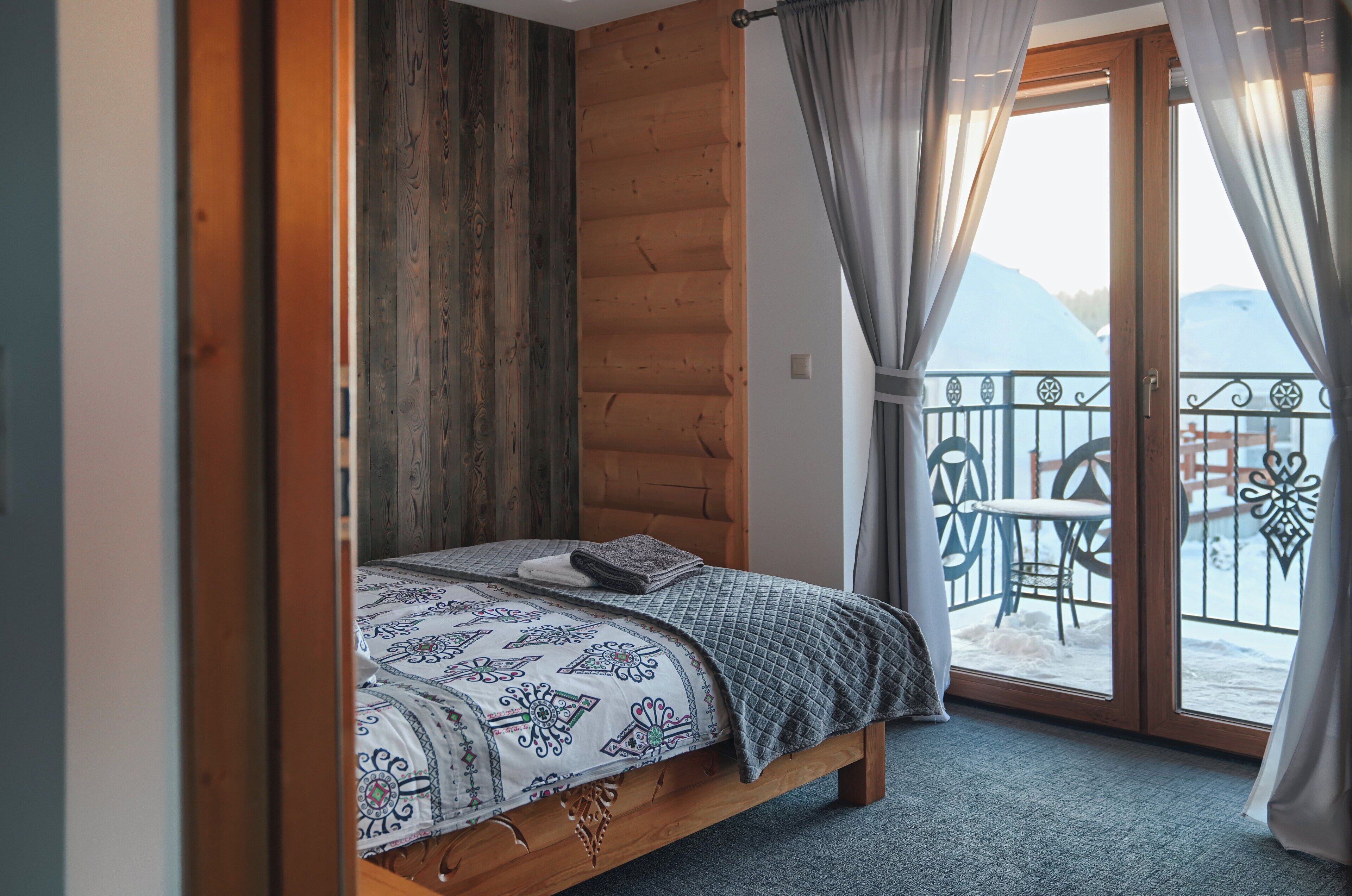 Ein Schlafzimmer mit einem hölzernen Kopfende, einem Bett mit gemusterten Textilien und einem Balkon mit Metallgeländer und Gartenmöbeln.