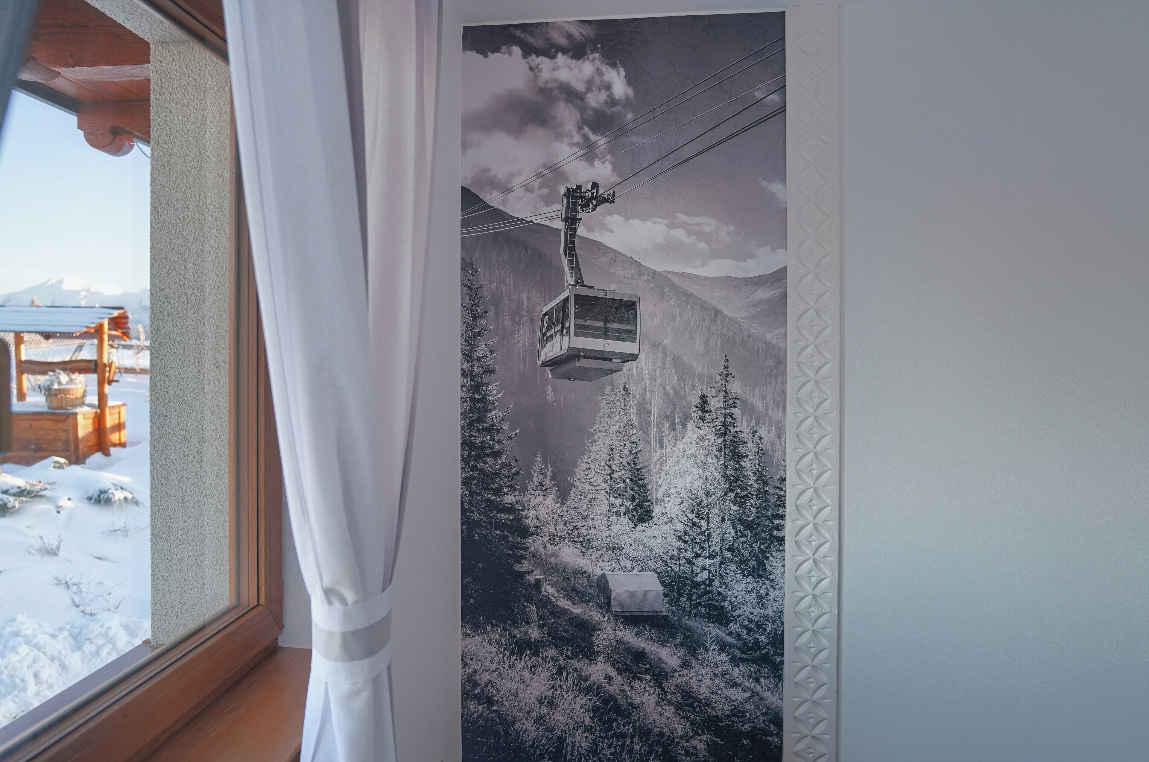 Ein Fenster mit Blick auf eine Berglandschaft, eine Seilbahn und eine Holzhütte.