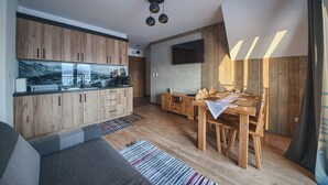 Eine moderne Küche mit Holzausstattung, ein Essbereich mit Holztisch und Stühlen sowie ein flachbildfernseher an der Wand.