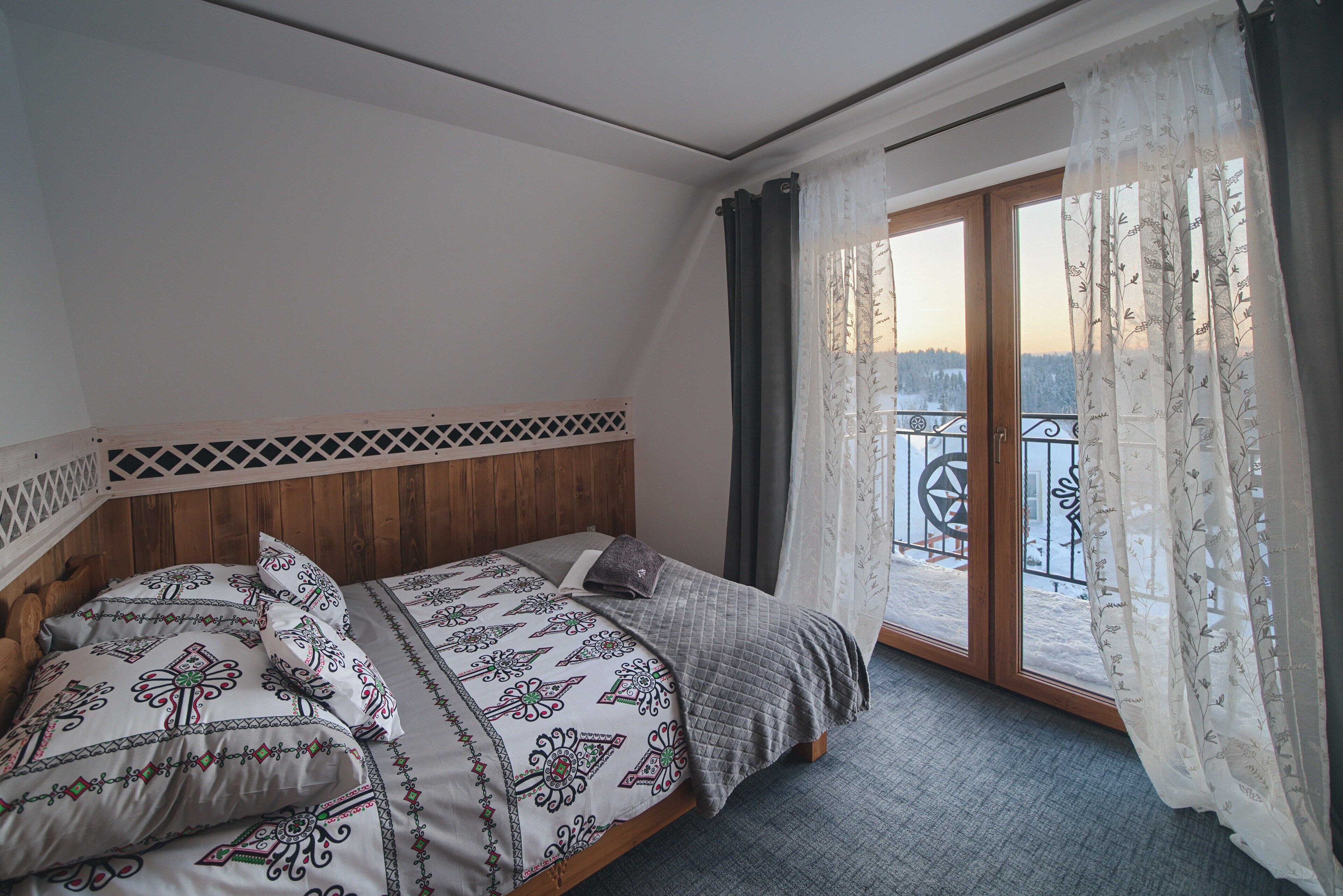 A bedroom with a wooden headboard, a large bed with patterned bedding, and a view of a balcony with a railing.