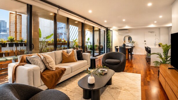 A modern living room with a sofa, armchairs, a coffee table, and a dining area with a kitchen in the background. - 3 Bedroom, Stylish, Spacious Stunner! Huge Balcony, Minutes to Marvel! (Melbourne)