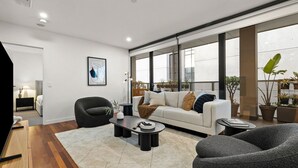 A modern living room with a sofa, armchairs, and a coffee table. There is a large window with a view of the city. - 3 Bedroom, Stylish, Spacious Stunner! Huge Balcony, Minutes to Marvel! (Melbourne)