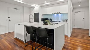 A modern kitchen with white cabinetry, a central island with bar stools, a built-in stove, and a backsplash. - 3 Bedroom, Stylish, Spacious Stunner! Huge Balcony, Minutes to Marvel! (Melbourne)